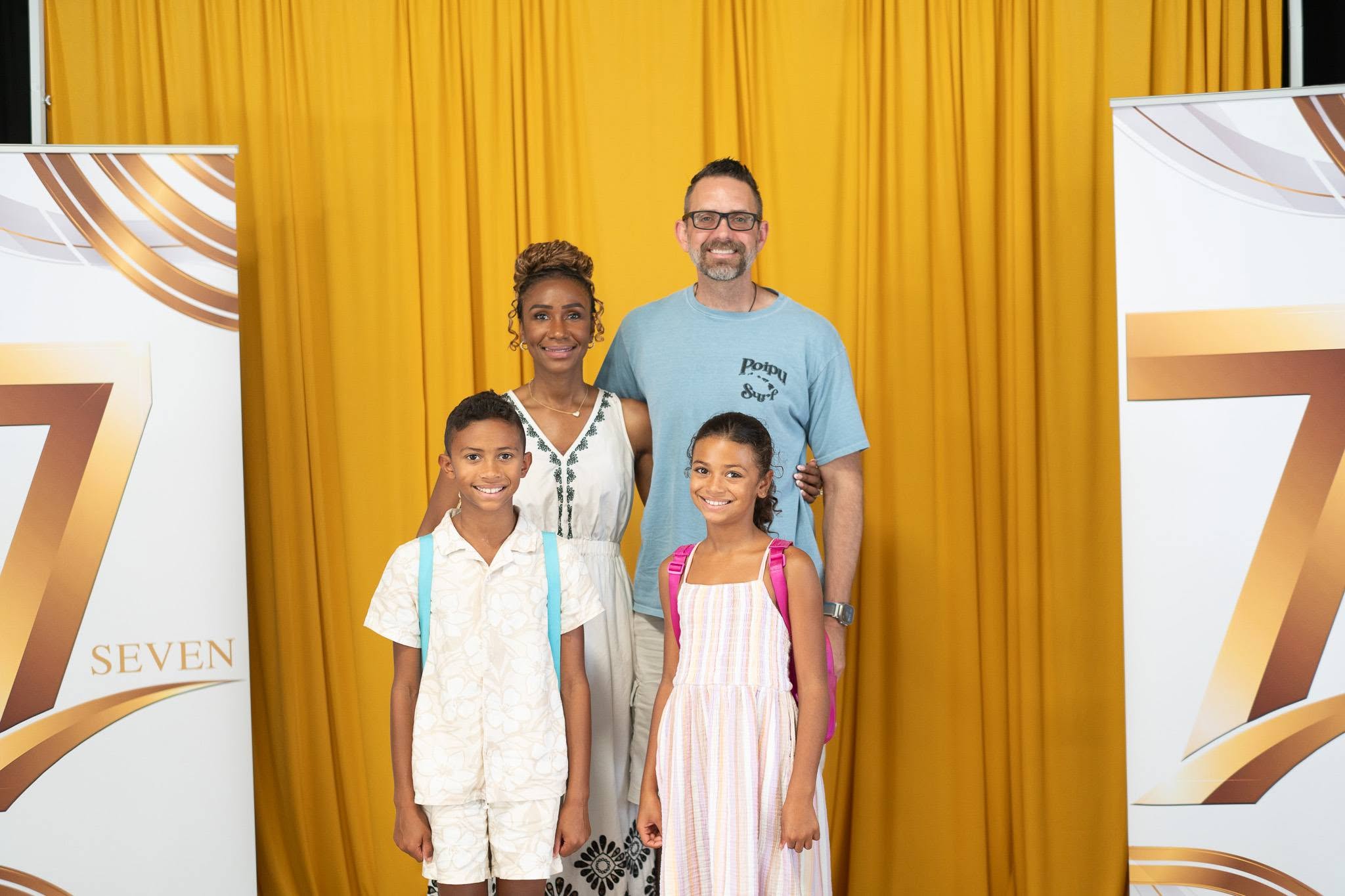 A family of four standing together in front of the gold Seven backdrop.