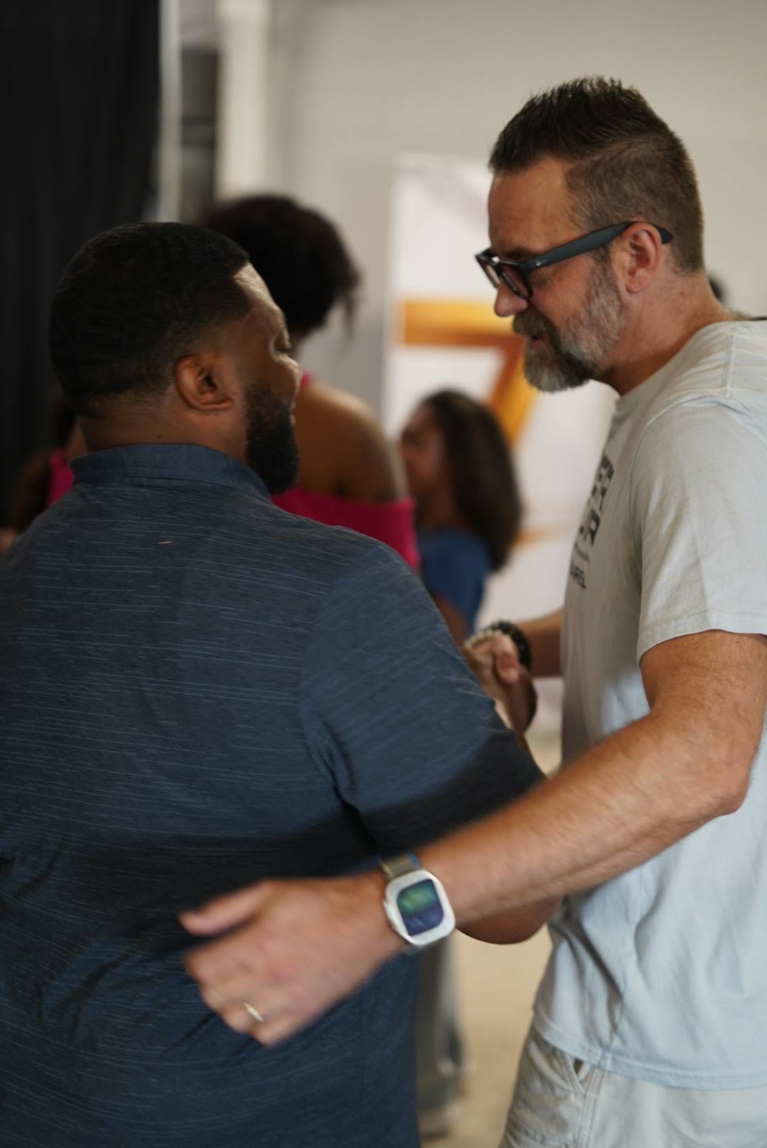 Pastor Heanon Tate greeting a man, with the gold Seven mark behind them.
