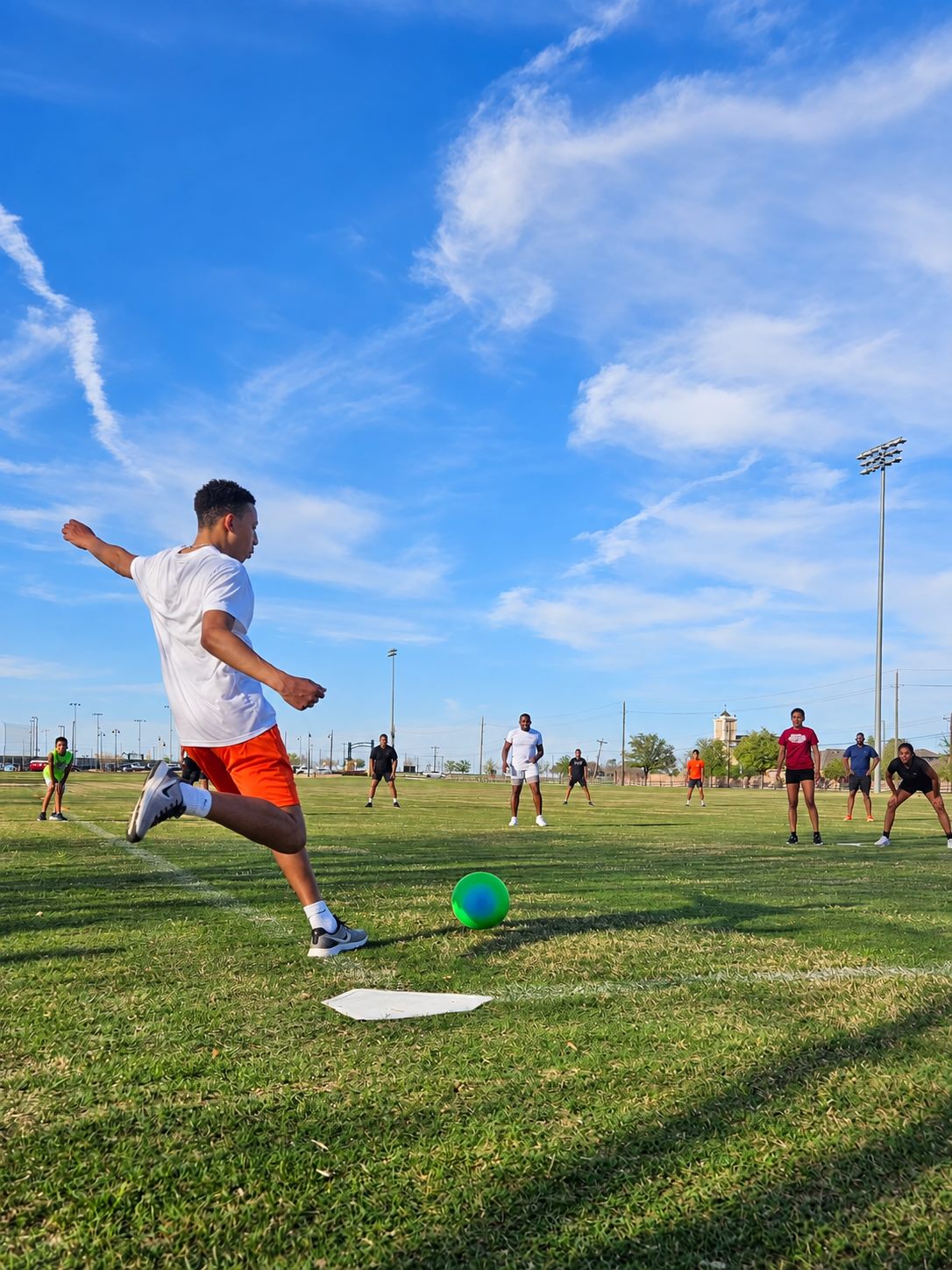 A player kicking off a kickball game on a sunny field.